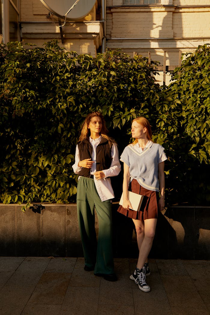 Two young women standing and talking casually outside in warm sunlight.